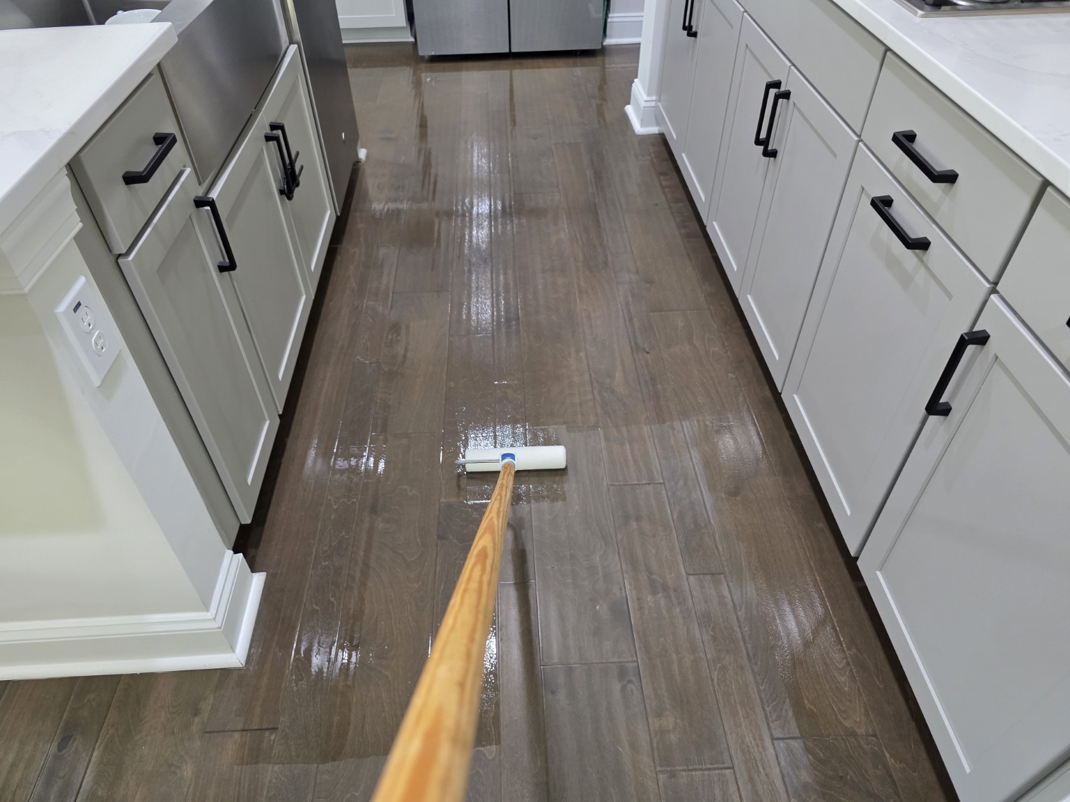 Fresh protective finish being applied to engineered hardwood kitchen floor