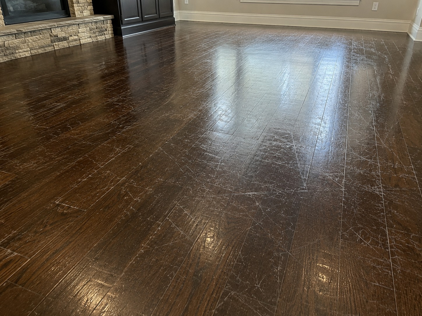 Dark hardwood floor with heavy scratching visible in the acrylic floor polish